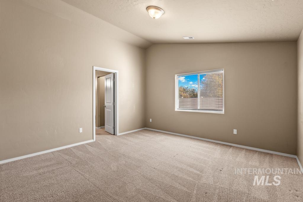 Spare room with lofted ceiling, light colored carpet, and a textured ceiling