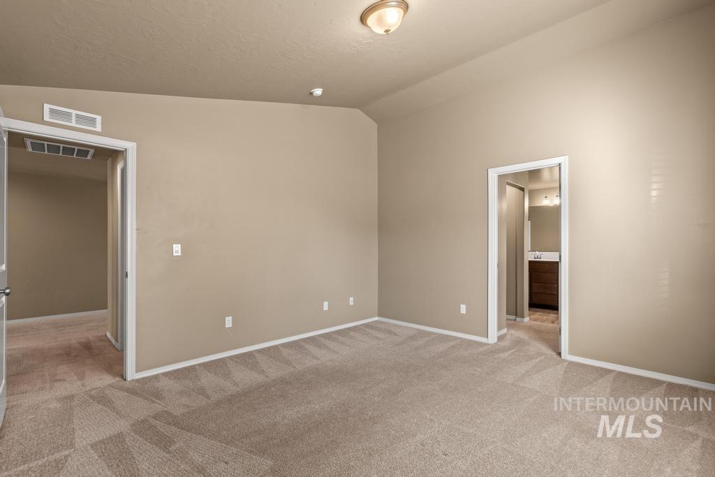 Unfurnished bedroom with lofted ceiling, light carpet, ensuite bath, and a textured ceiling