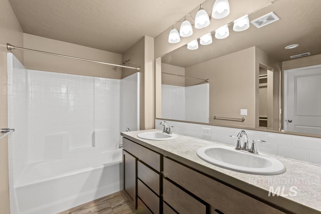 Full bath with light wood-type flooring, tub / shower combination, double vanity, and a textured ceiling