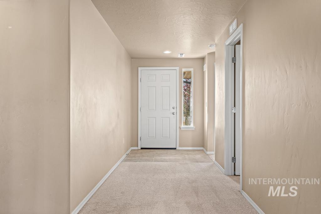 Hallway with light colored carpet and a textured ceiling