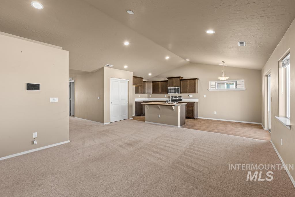 Kitchen featuring open floor plan, light countertops, light carpet, a kitchen breakfast bar, and vaulted ceiling