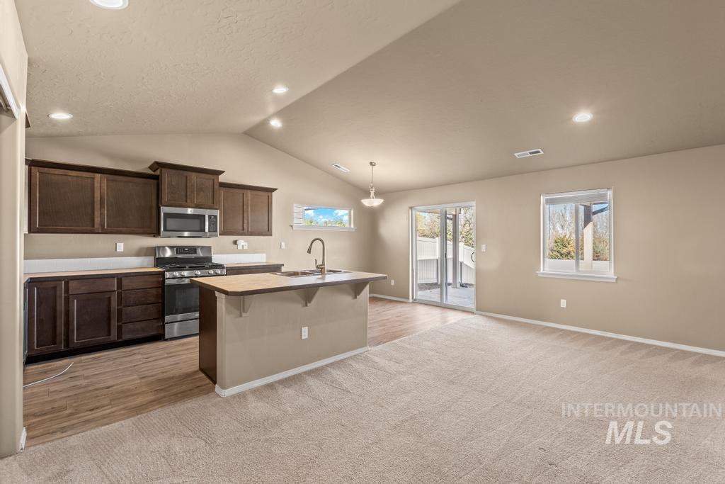 Kitchen featuring a kitchen bar, appliances with stainless steel finishes, light carpet, a kitchen island with sink, and recessed lighting