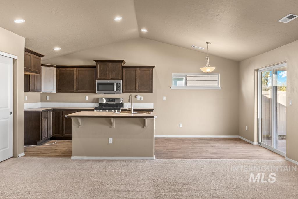 Kitchen featuring a breakfast bar area, lofted ceiling, appliances with stainless steel finishes, a kitchen island with sink, and dark brown cabinets