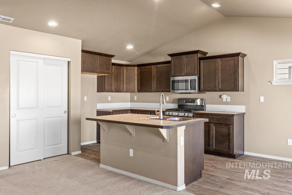 Kitchen with a breakfast bar, dark brown cabinets, stainless steel appliances, recessed lighting, and vaulted ceiling