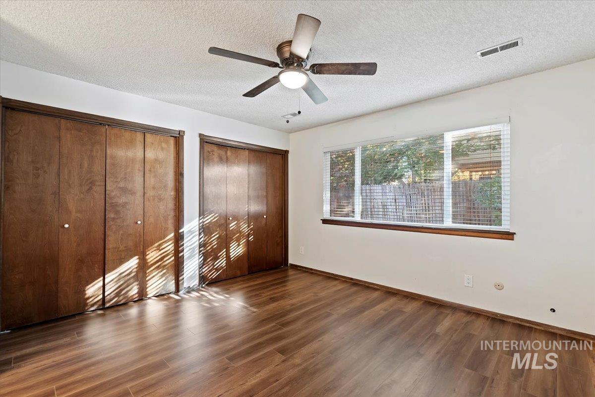 Unfurnished bedroom with two closets, dark wood-style floors, a textured ceiling, and a ceiling fan