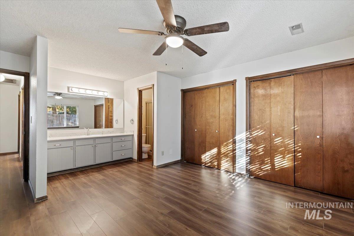 Unfurnished bedroom with a textured ceiling, multiple closets, dark wood-style flooring, and ceiling fan