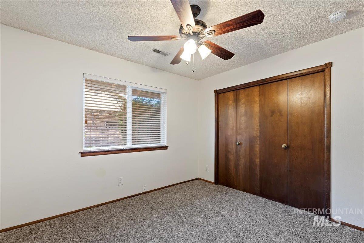 Unfurnished bedroom featuring a textured ceiling, a closet, carpet flooring, and ceiling fan