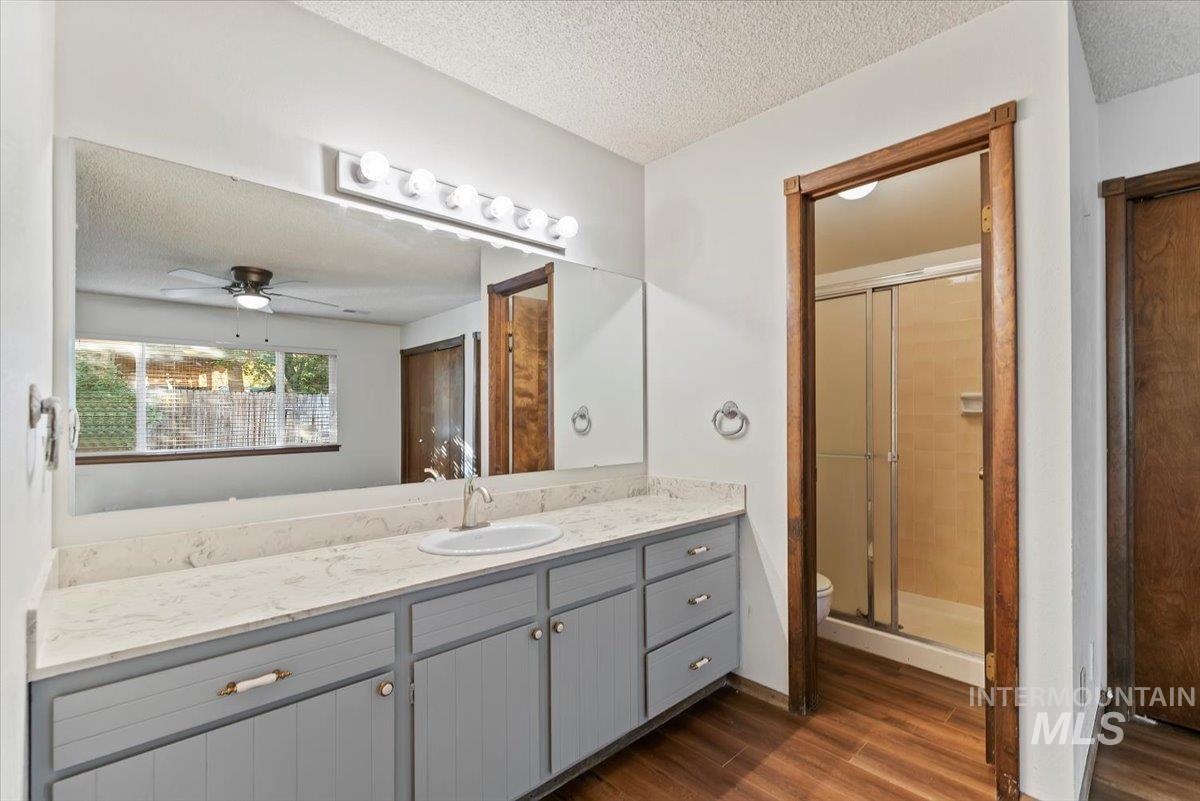 Bathroom with a textured ceiling, vanity, dark wood-style floors, a shower stall, and a ceiling fan