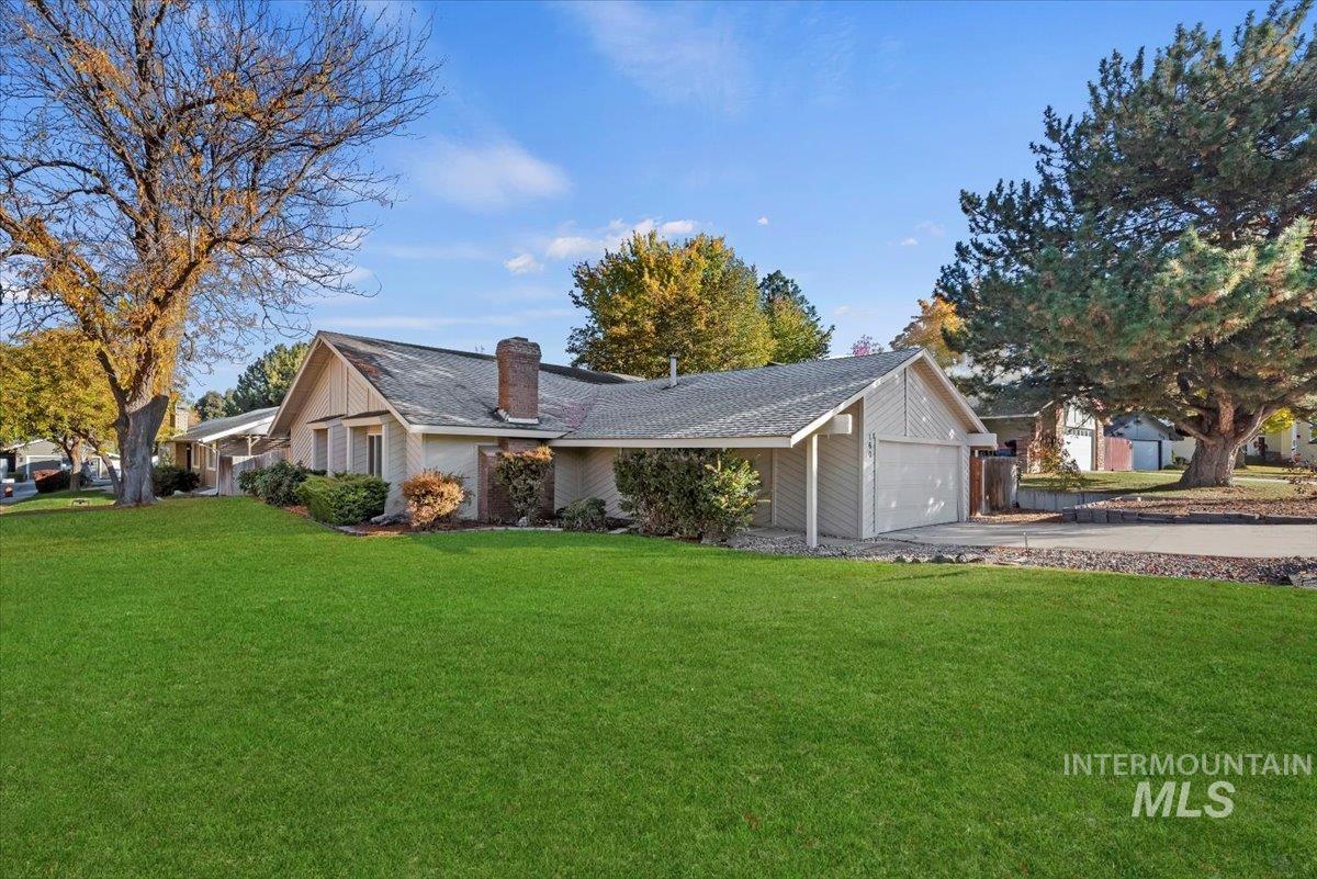 View of front of house with a front yard, a chimney, driveway, an attached garage, and a shingled roof
