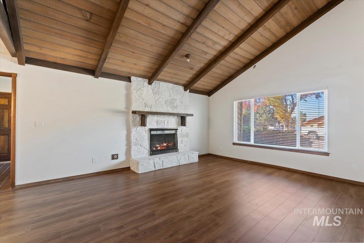 Unfurnished living room with a wood ceiling with exposed beams, a stone fireplace, dark wood-style floors, and high vaulted ceiling