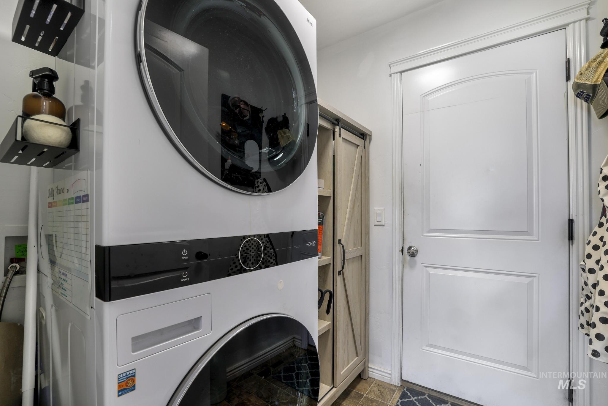 Laundry room with stacked washing machine and dryer and a barn door