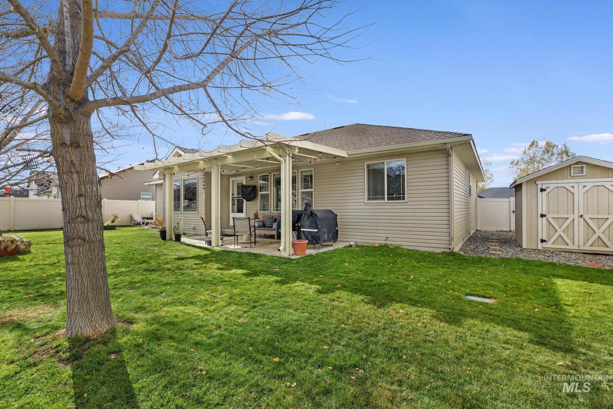 Back of house with a fenced backyard, a storage unit, a patio area, and roof with shingles