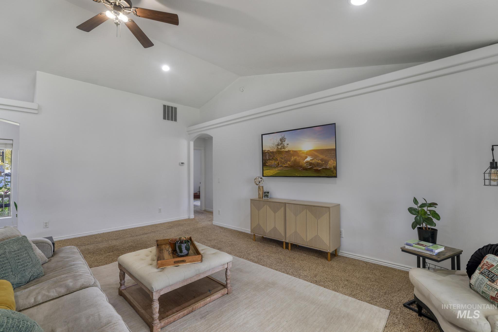 Living area with carpet flooring, vaulted ceiling, arched walkways, a ceiling fan, and recessed lighting
