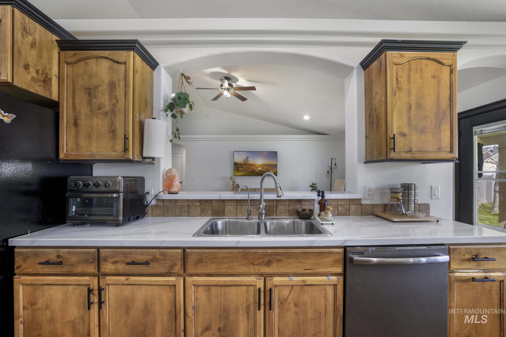 Kitchen featuring stainless steel dishwasher, brown cabinets, lofted ceiling, a ceiling fan, and light stone countertops