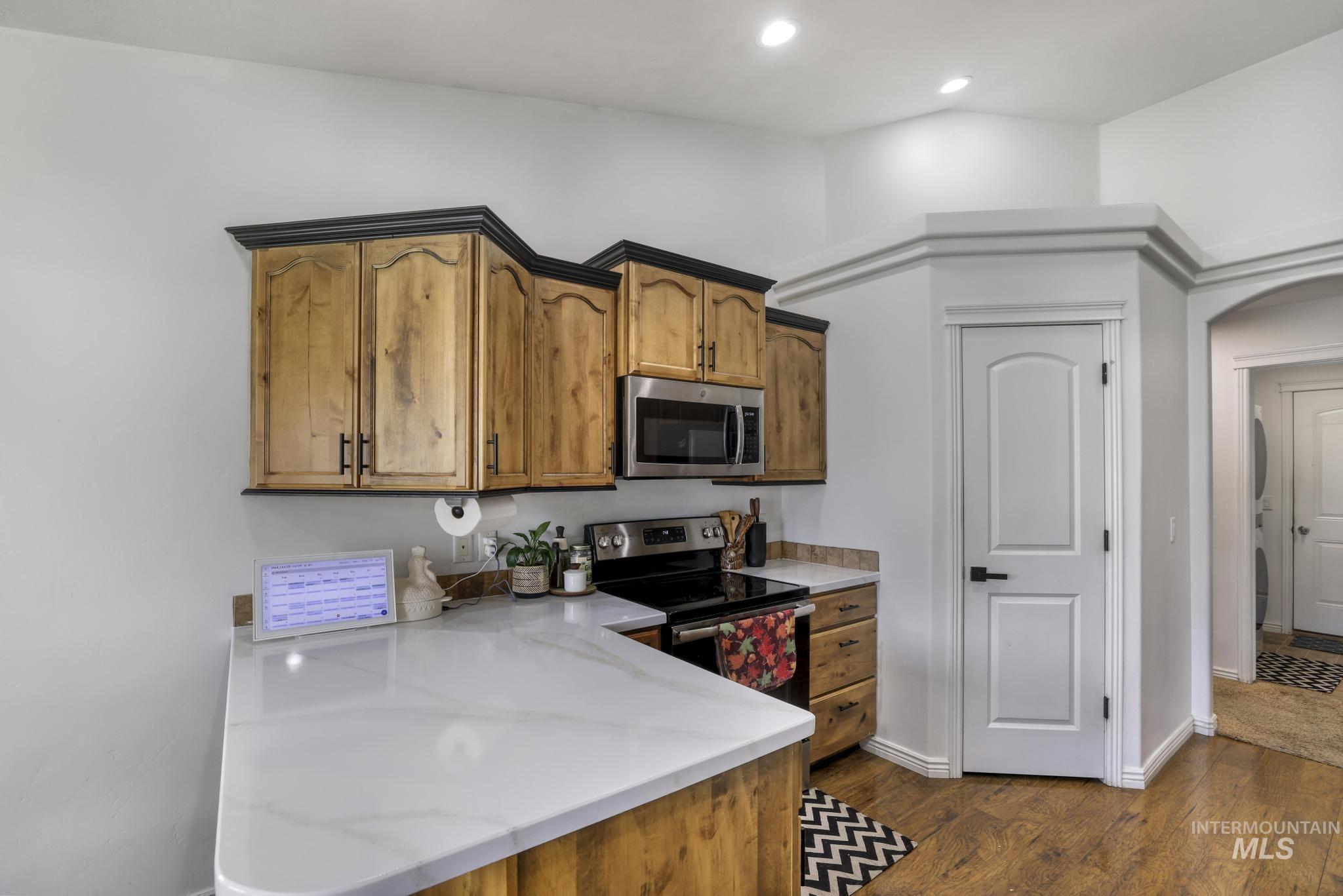 Kitchen featuring appliances with stainless steel finishes, dark wood-style floors, light stone counters, brown cabinetry, and recessed lighting