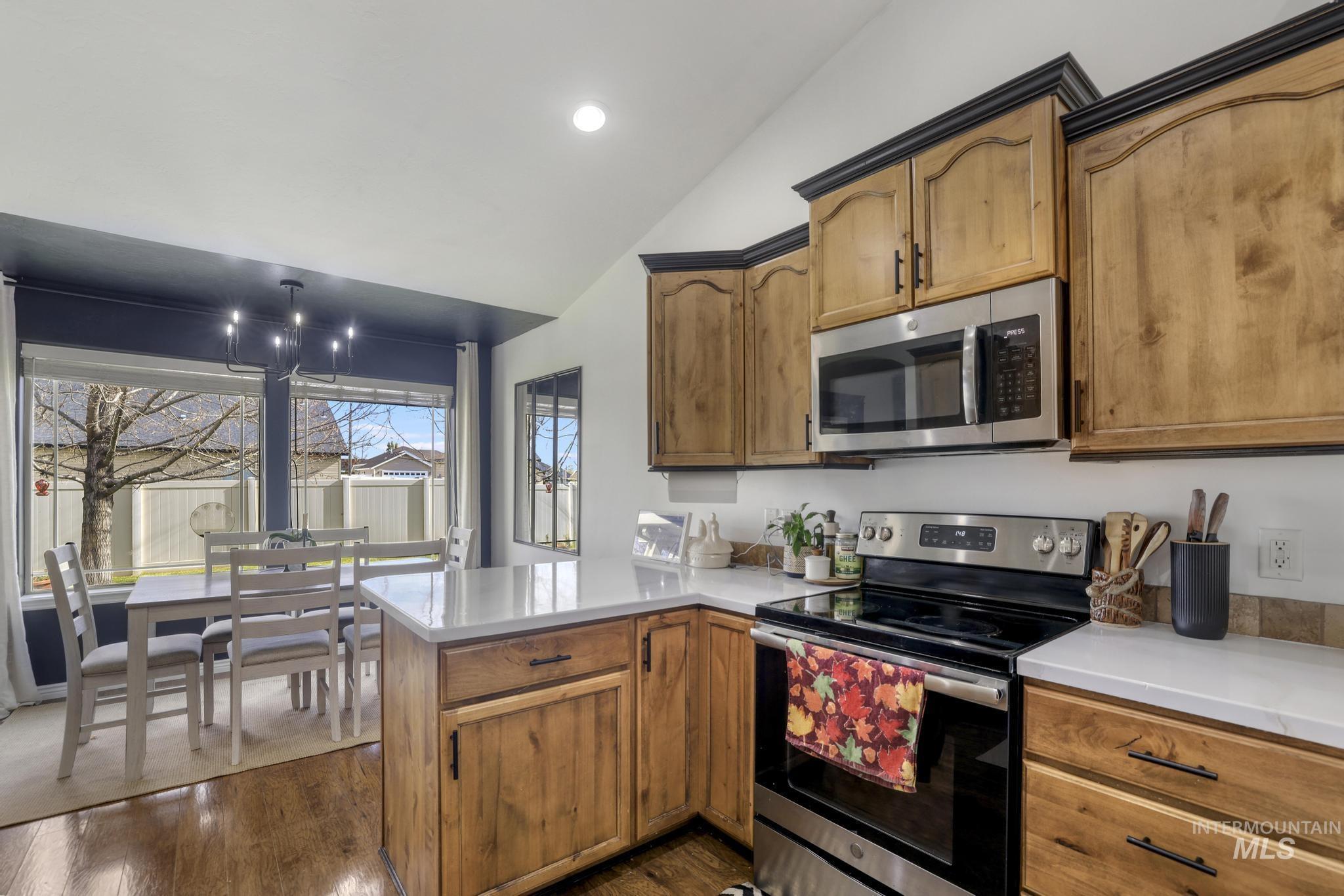 Kitchen with stainless steel appliances, lofted ceiling, dark wood finished floors, a peninsula, and brown cabinets