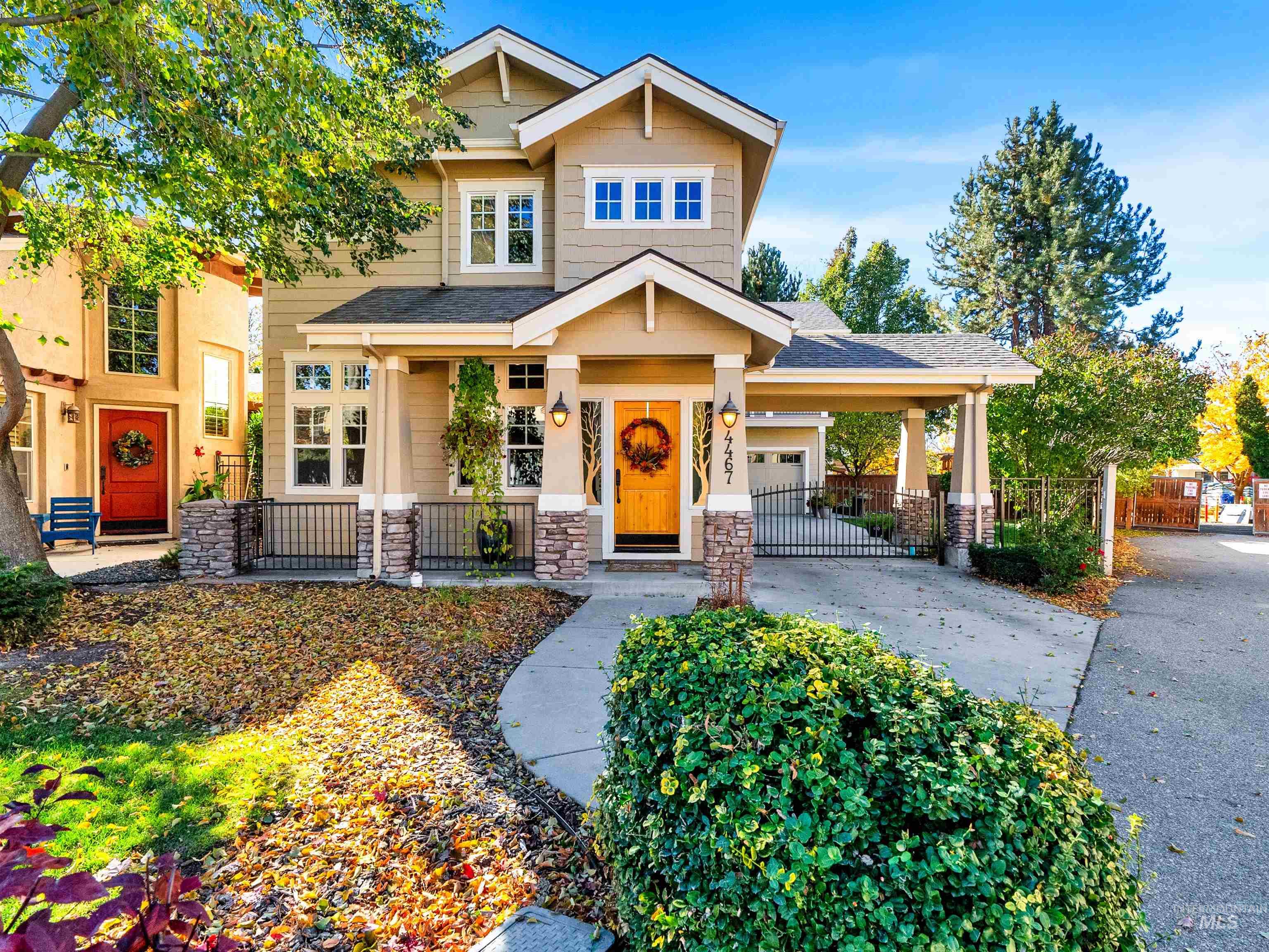 Craftsman-style home featuring stone siding, covered porch, driveway, a shingled roof, and a gate