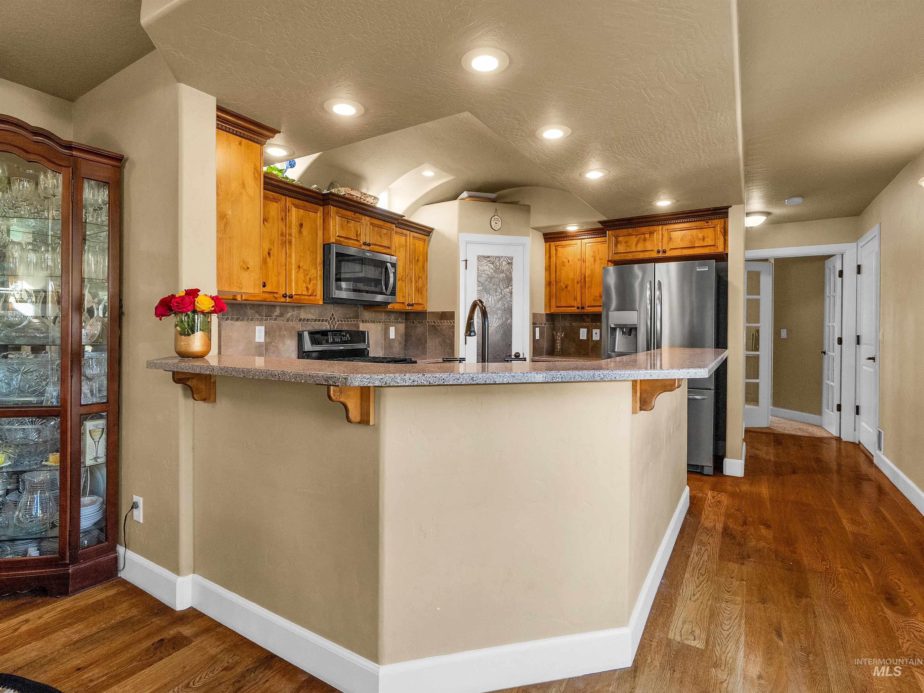 Kitchen featuring a kitchen breakfast bar, decorative backsplash, a peninsula, brown cabinetry, and a textured ceiling