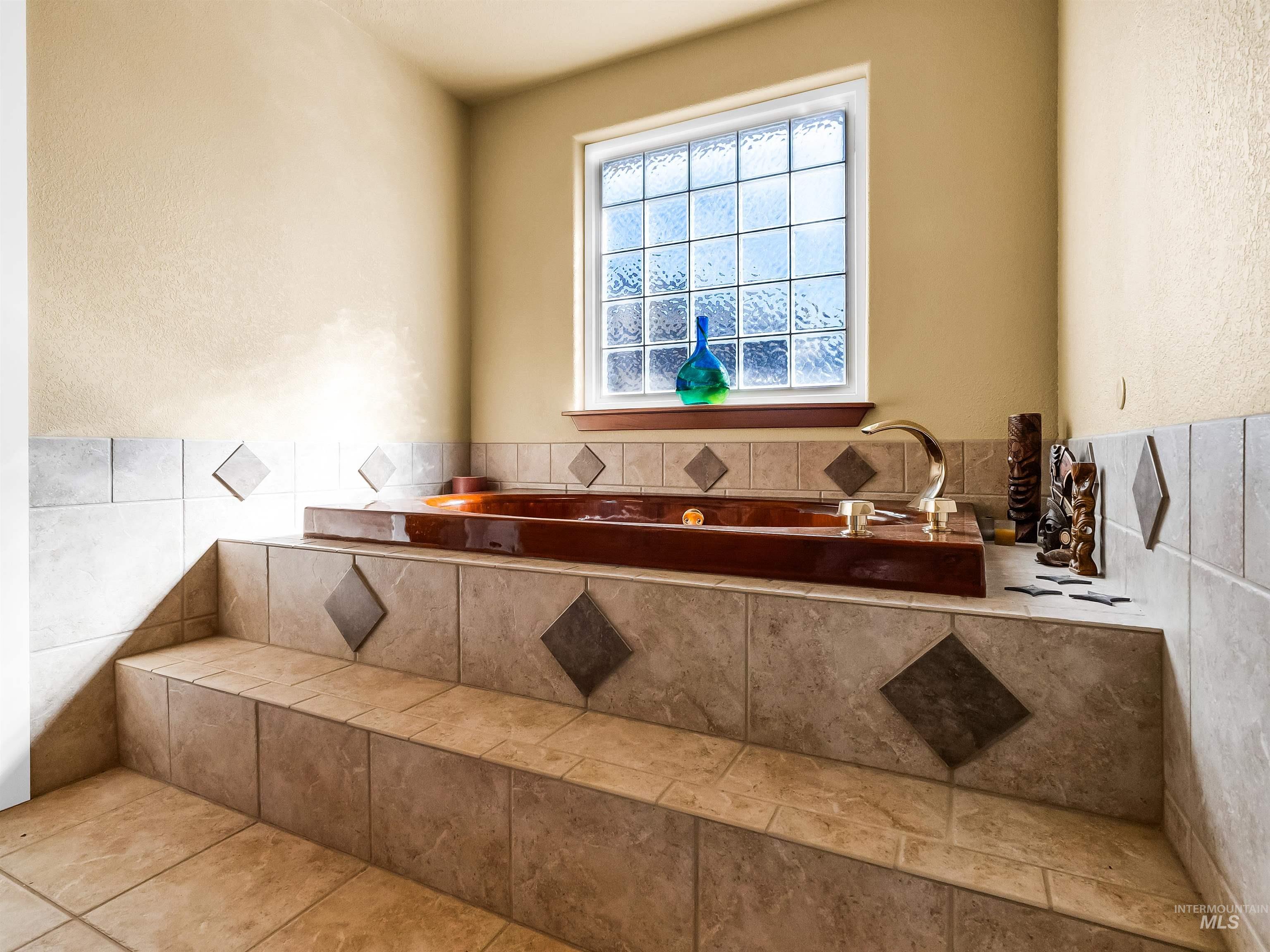 Full bath featuring a textured wall, tile walls, a garden tub, tile patterned flooring, and wainscoting