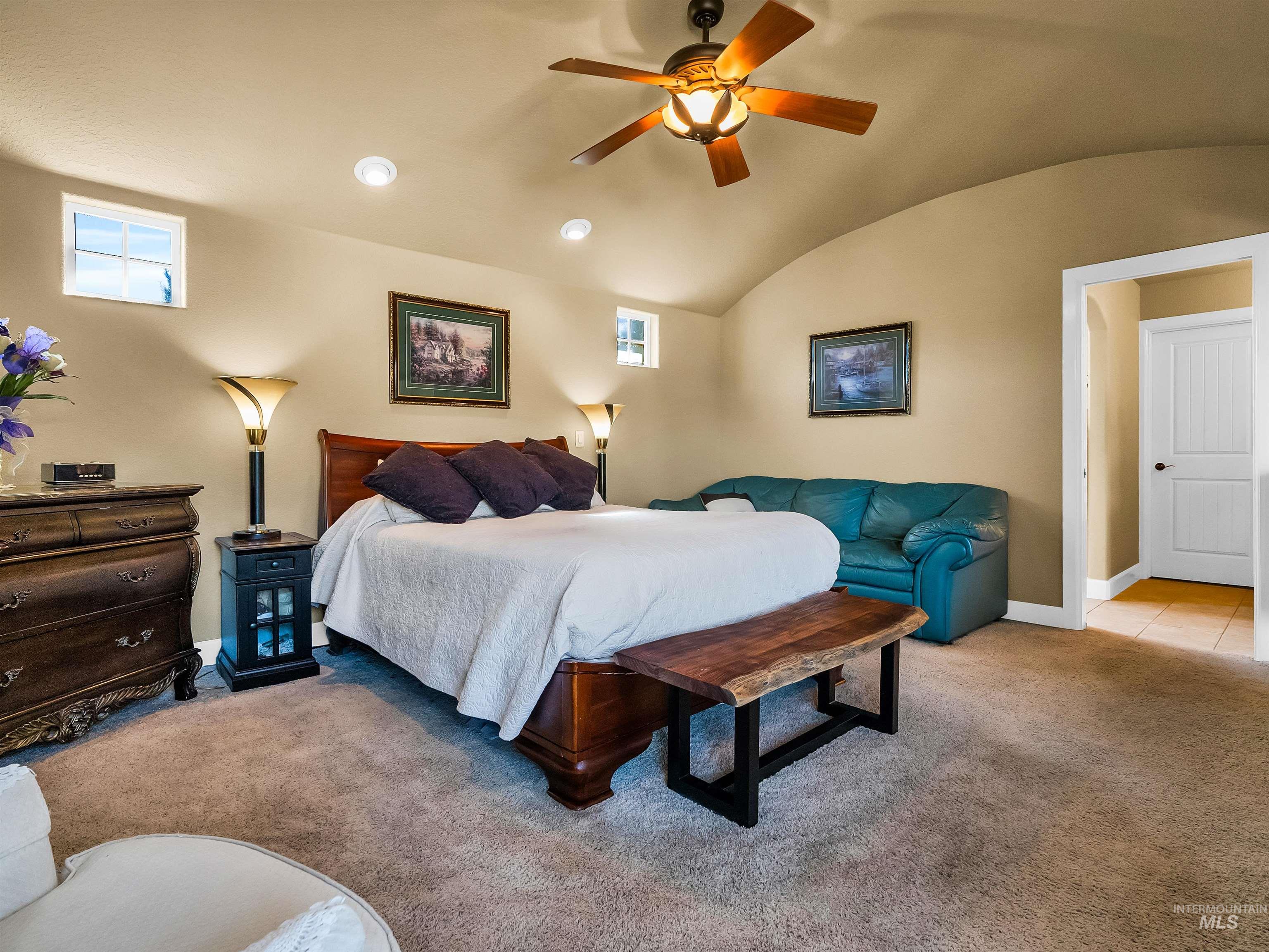 Bedroom featuring vaulted ceiling, light colored carpet, multiple windows, and a ceiling fan