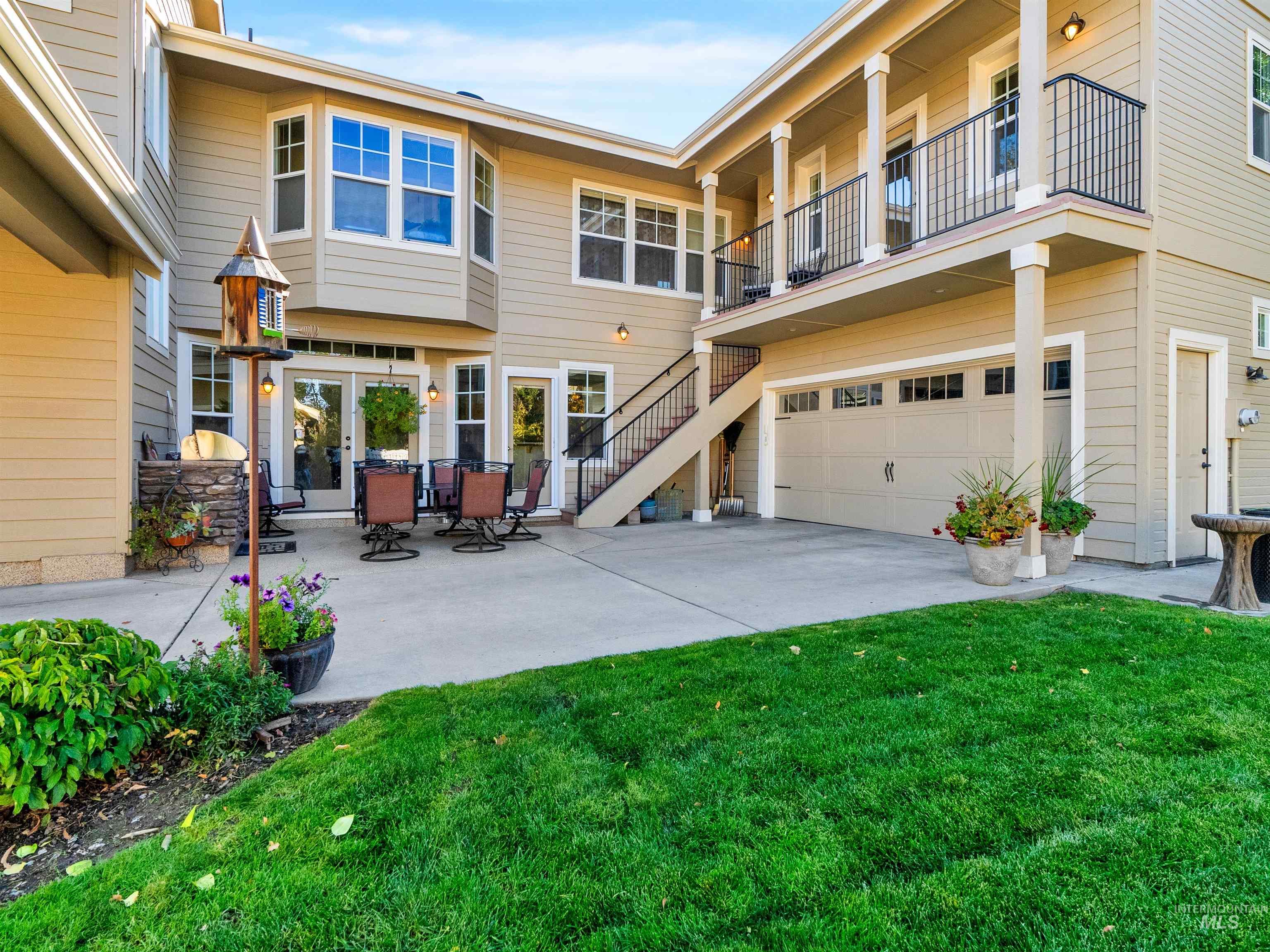 Back of house with stairs, a patio area, a lawn, and a balcony