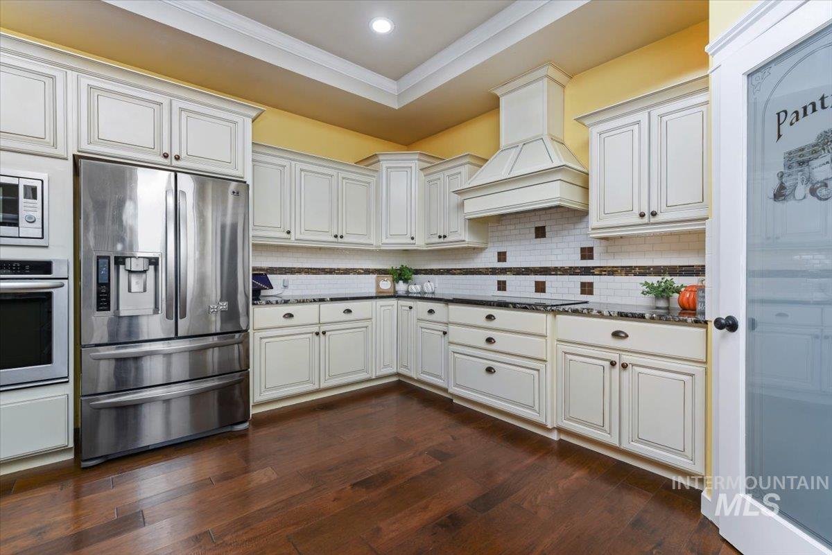 Kitchen featuring appliances with stainless steel finishes, backsplash, dark wood finished floors, stone countertops, and crown molding