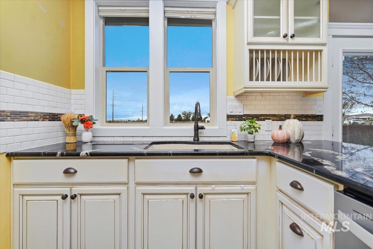Kitchen with glass insert cabinets, decorative backsplash, dishwasher, cream cabinetry and pantry.