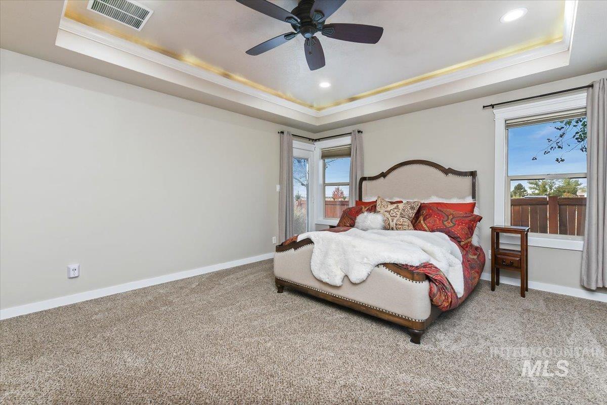 Carpeted bedroom with a tray ceiling, multiple windows, a ceiling fan, and recessed lighting