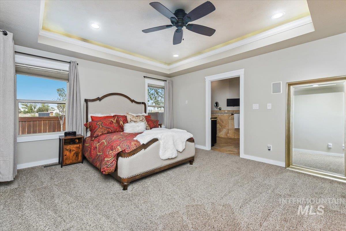 Carpeted bedroom featuring a tray ceiling, a ceiling fan, recessed lighting, connected bathroom, and crown molding