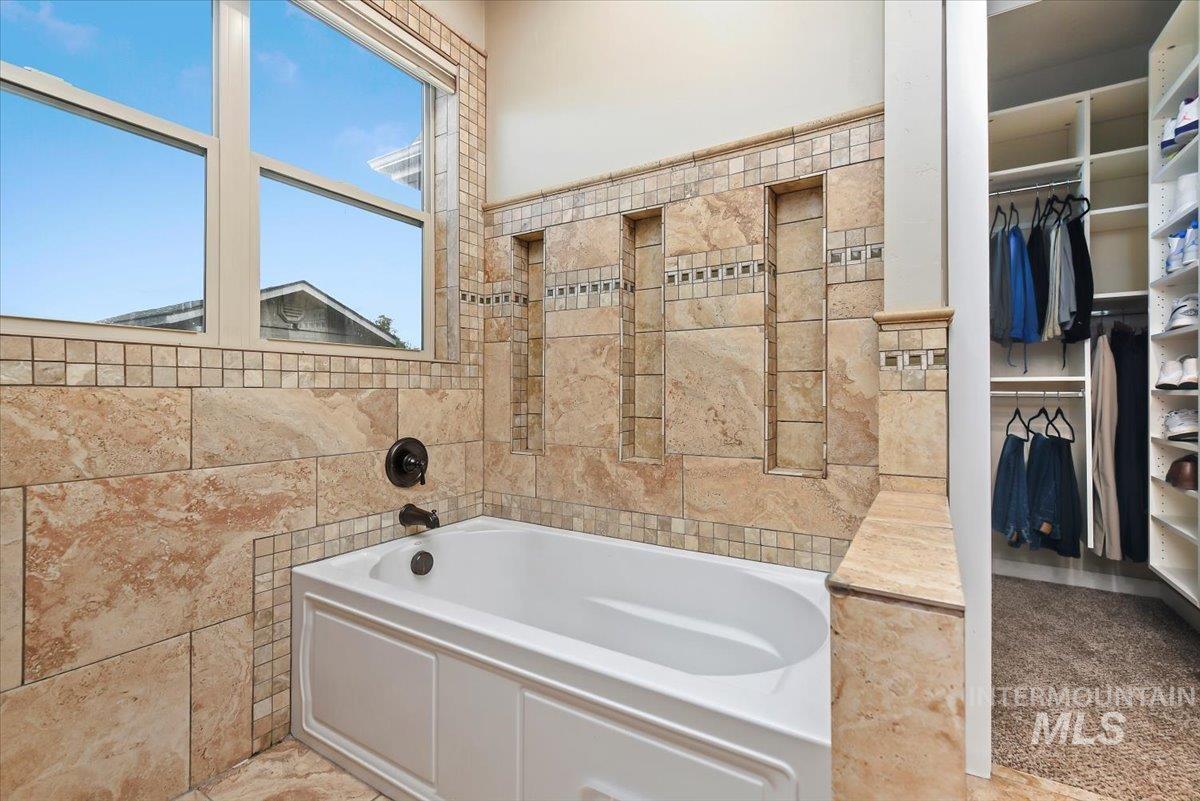Bathroom with a garden tub, a spacious closet, and tile walls