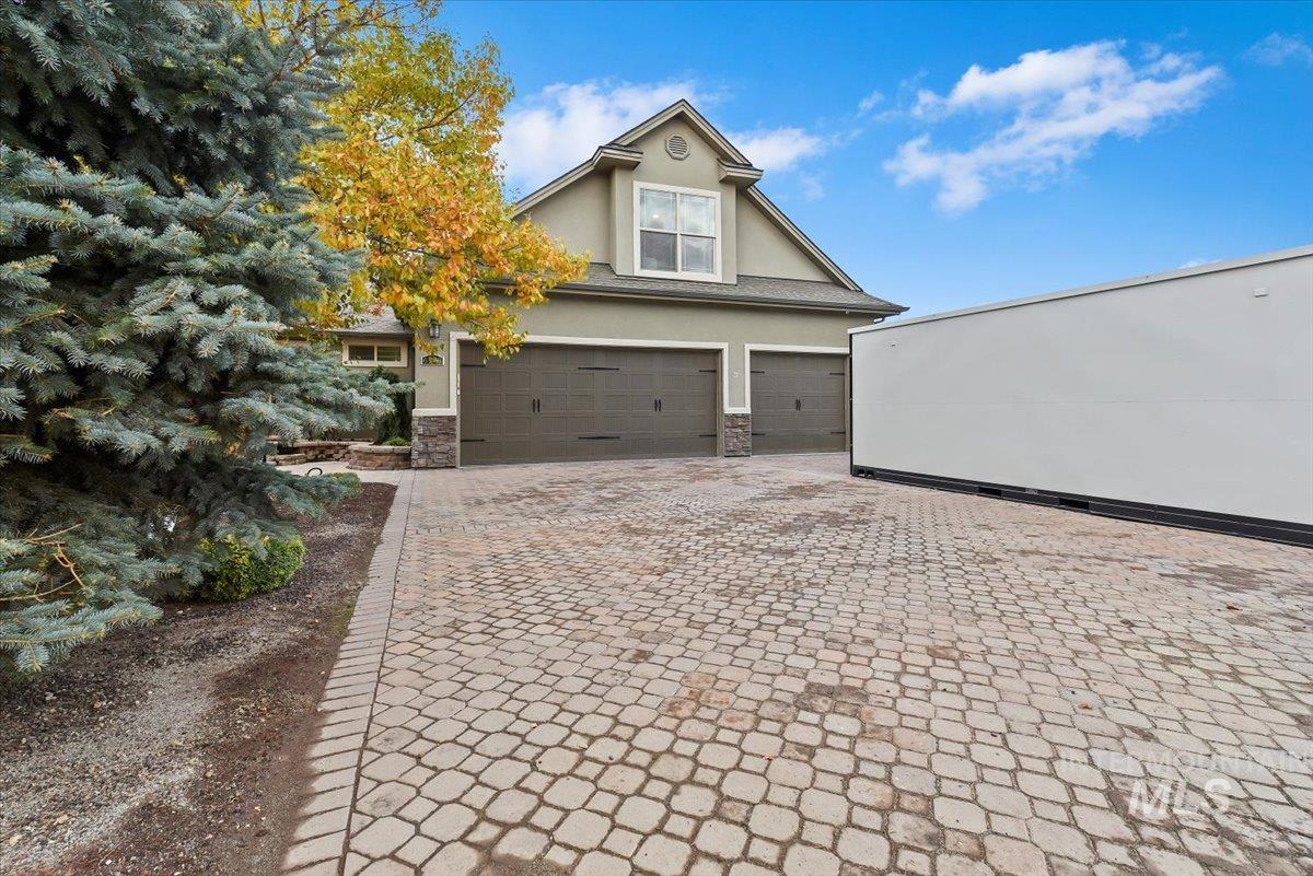 View of front facade featuring stucco siding, decorative driveway, an attached garage, and stone siding