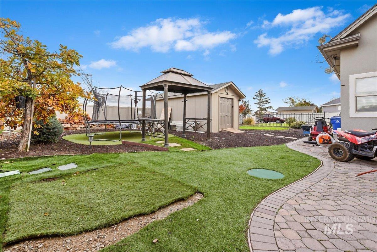 View of playyard with a trampoline, and an outdoor storage building for your toys, and lawn equipemnt