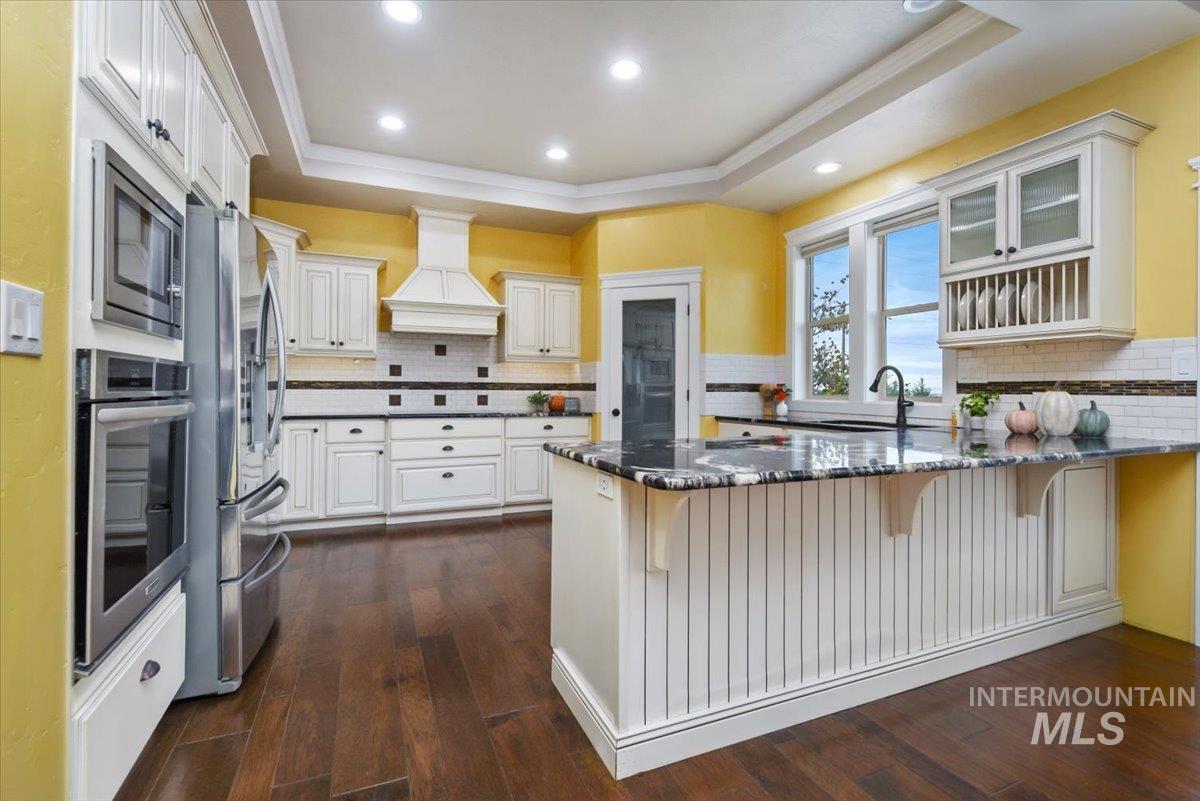 Kitchen featuring a raised ceiling, wood-type flooring, a breakfast bar area, tasteful backsplash, recessed lighting and pantry