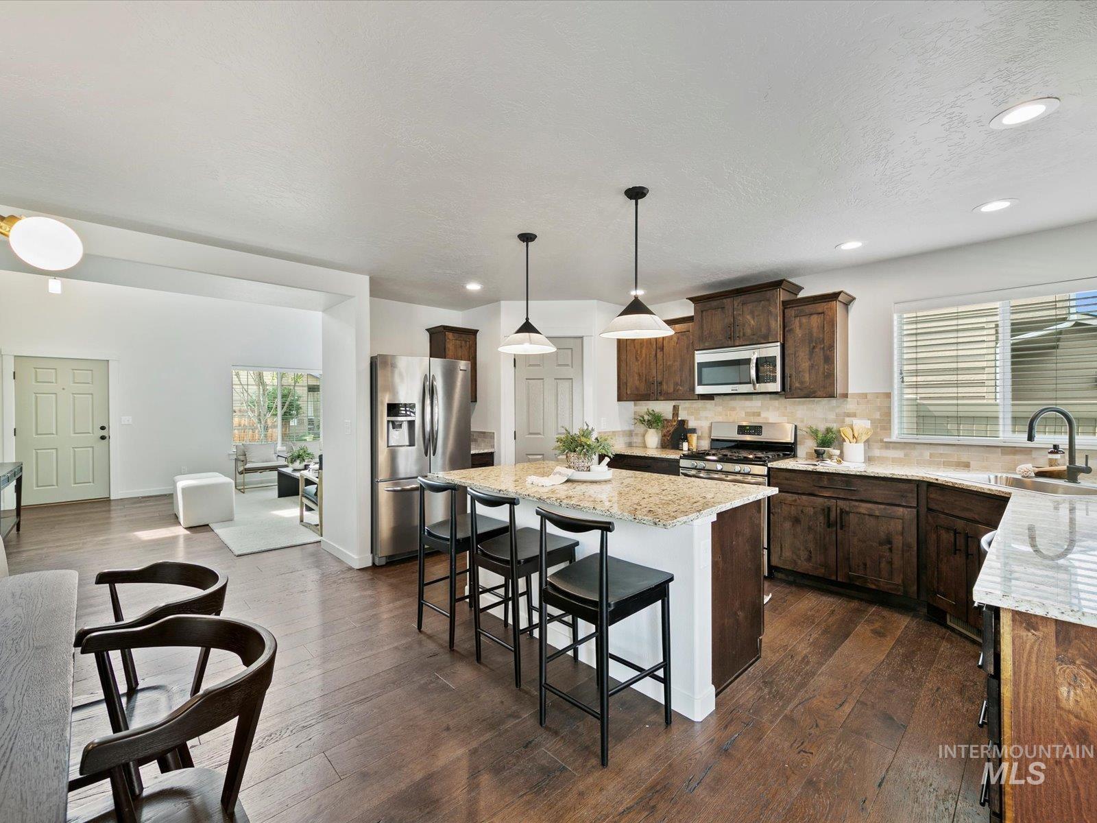 Kitchen featuring dark brown cabinets, stainless steel appliances, a kitchen island, hanging light fixtures, and light stone countertops