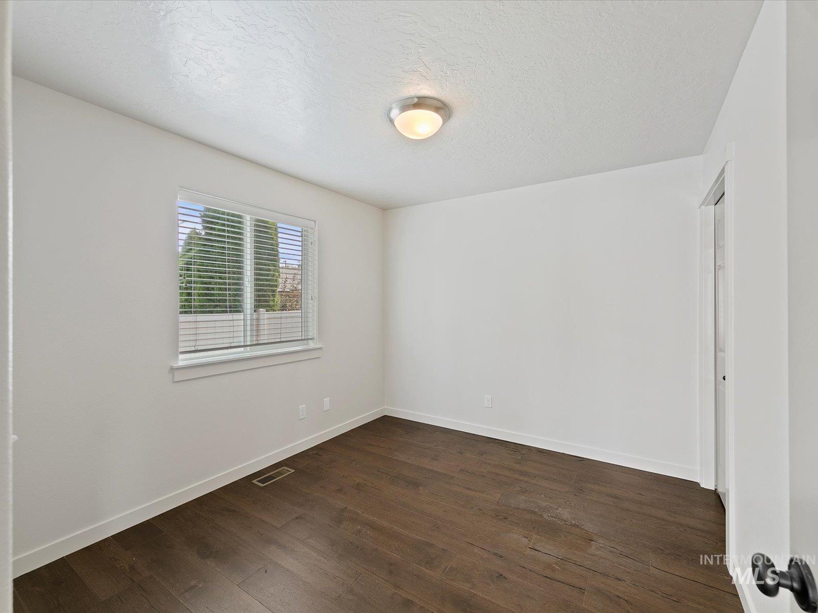 Spare room with a textured ceiling and dark wood-style flooring