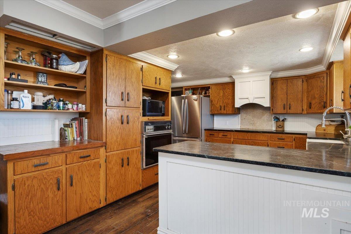 Kitchen featuring open shelves, crown molding, black appliances, dark wood-type flooring, and brown cabinets