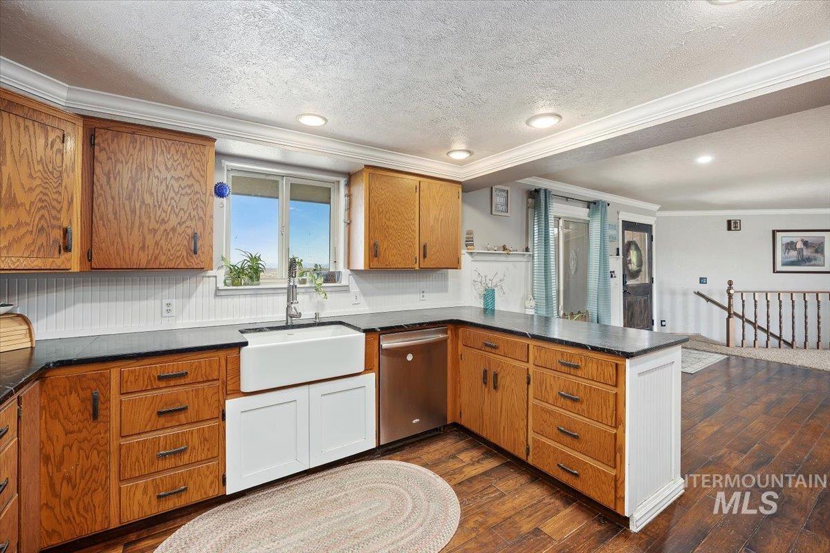 Kitchen featuring a peninsula, ornamental molding, dark wood-style floors, brown cabinets, and dishwasher