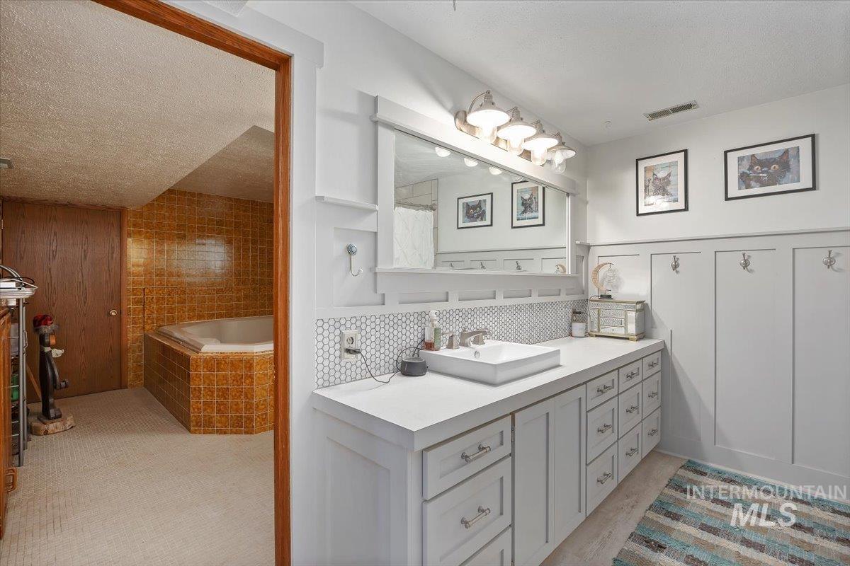 Bathroom with vanity, a textured ceiling, tiled bath, a shower with curtain, and wainscoting