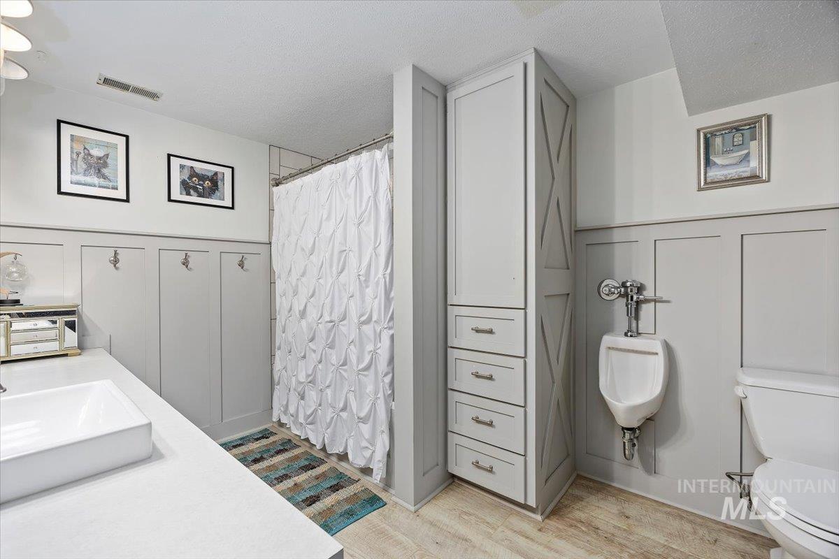 Full bathroom with a decorative wall, a wainscoted wall, a shower with shower curtain, light wood-type flooring, and a textured ceiling