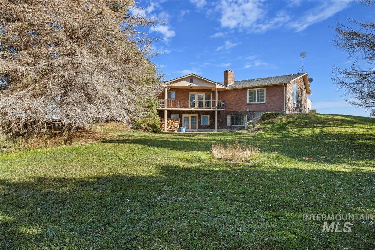 Rear view of property with a chimney, a yard, brick siding, a balcony, and a patio area