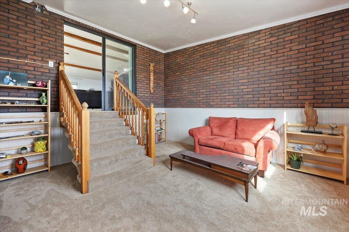 Sitting room featuring brick wall, a wainscoted wall, stairs, carpet, and ornamental molding