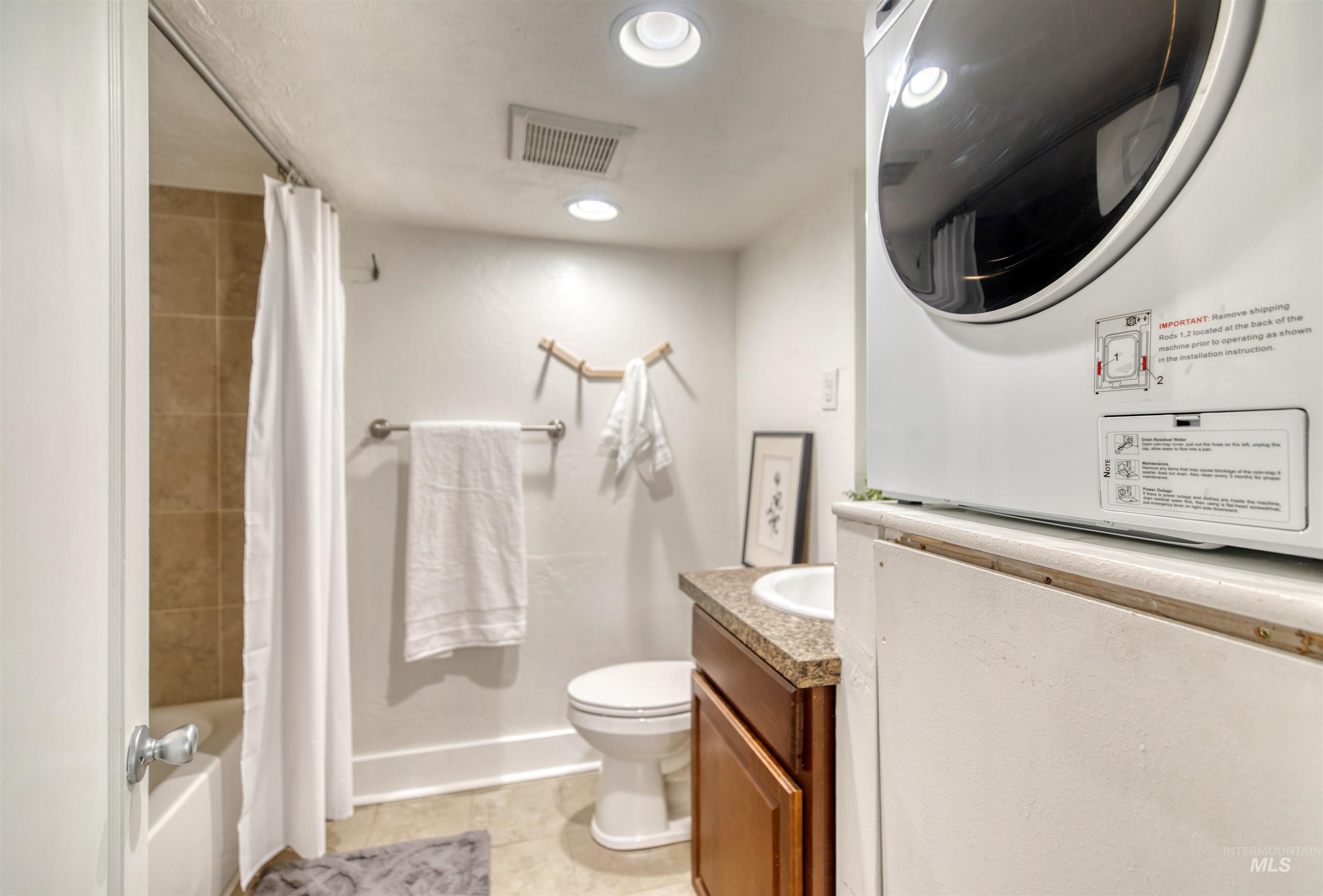 Full bathroom with light tile patterned floors, shower / bath combo with shower curtain, estacked washer and dryer, vanity, and recessed lighting