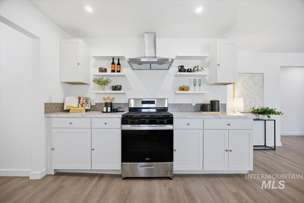 Kitchen with open shelves, white cabinets, stainless steel gas stove, exhaust hood, and light stone countertops
