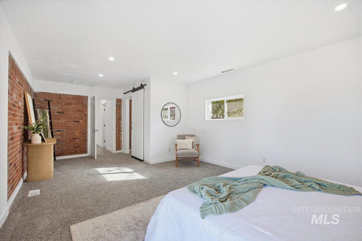 Bedroom featuring a barn door, carpet floors, brick wall, and recessed lighting