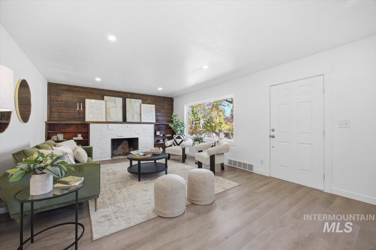 Living room with a brick fireplace, light wood finished floors, and recessed lighting