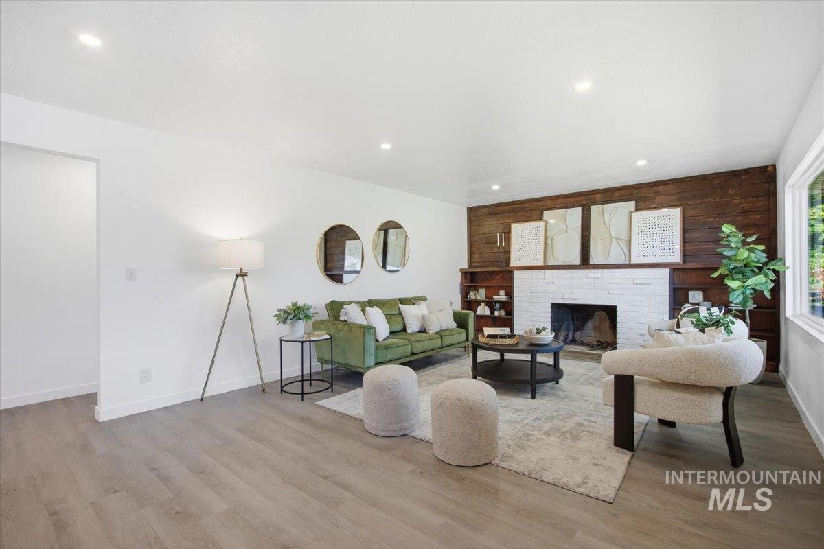 Living room featuring wooden walls, a brick fireplace, recessed lighting, and light wood-style floors