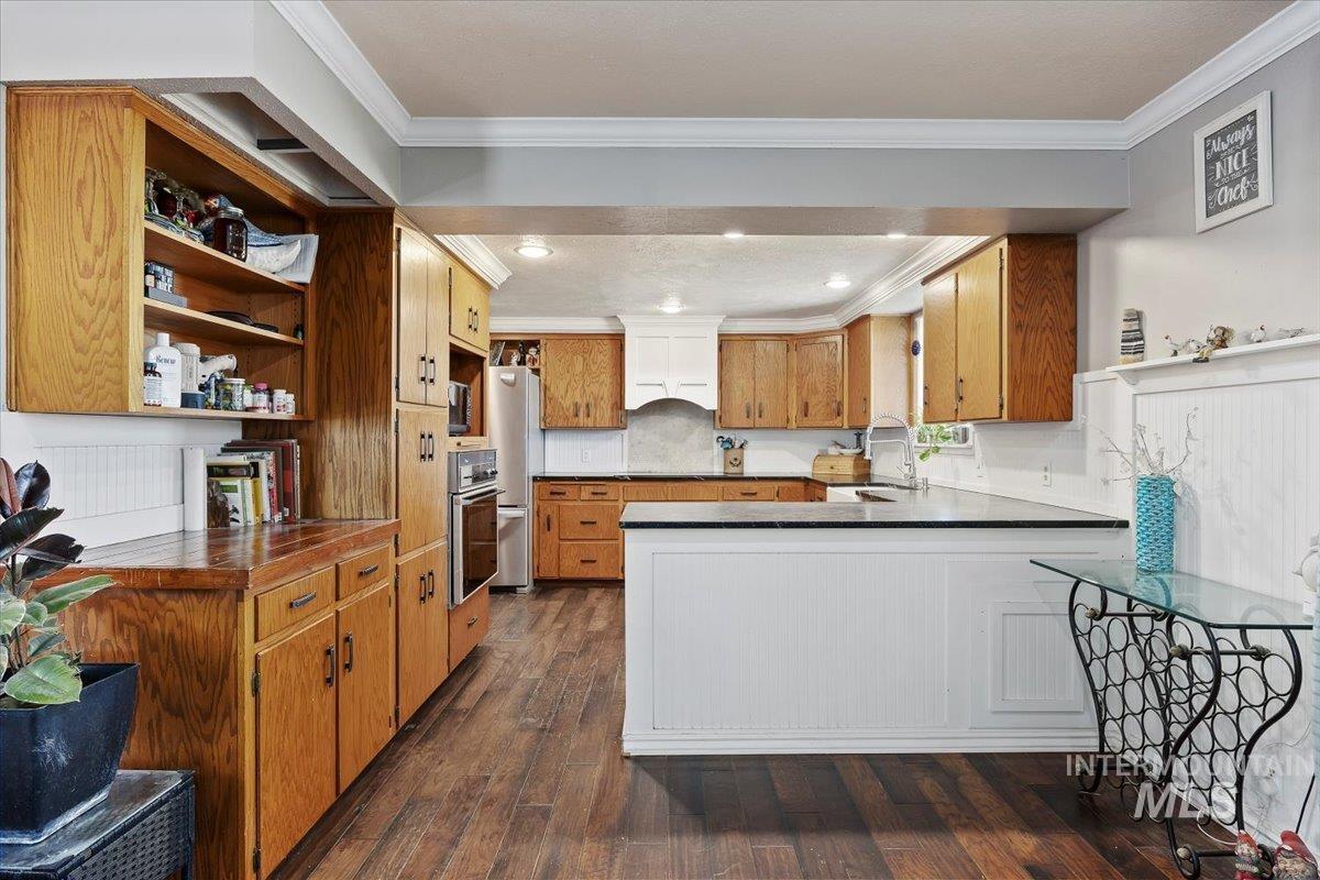 Kitchen with brown cabinets, dark wood-style floors, crown molding, a peninsula, and open shelves