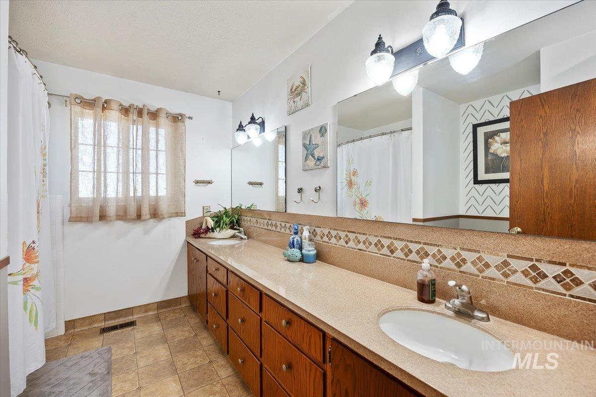 Full bath featuring curtained shower, double vanity, and backsplash