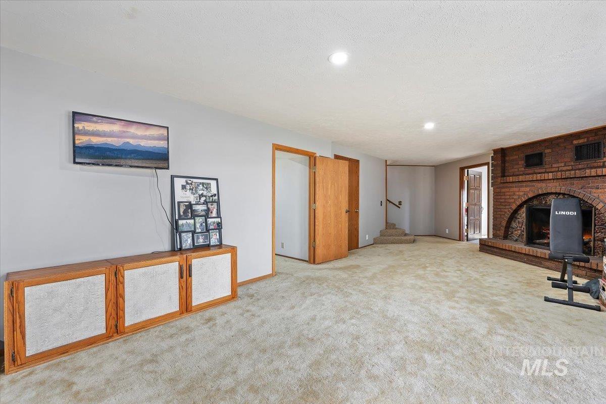 Unfurnished living room with a brick fireplace, carpet flooring, a textured ceiling, and recessed lighting