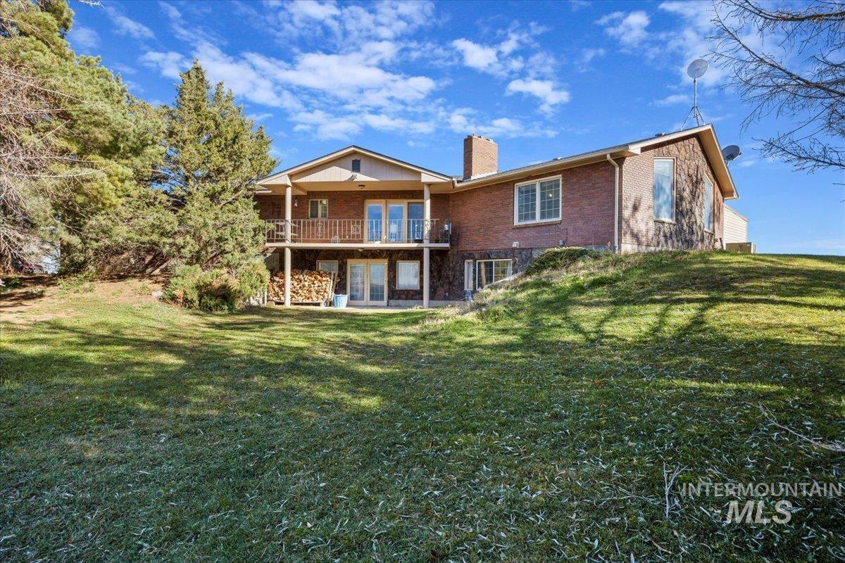 Rear view of property with brick siding, a chimney, a lawn, and a patio